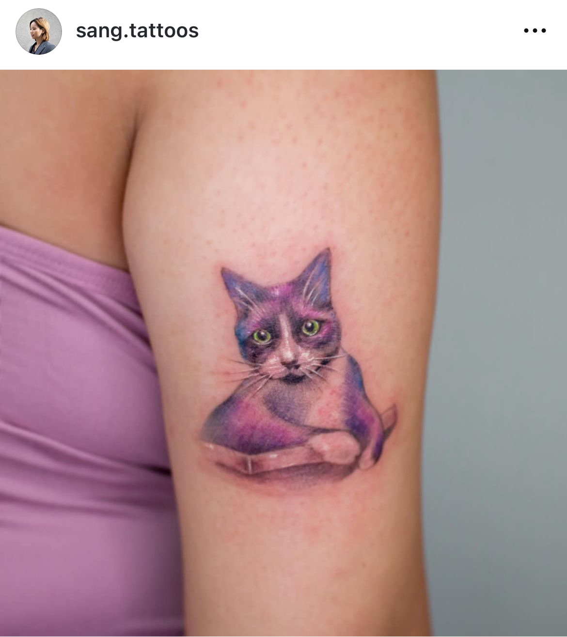 Colour watercolour-style tattoo of a purple and white cat on an upper arm