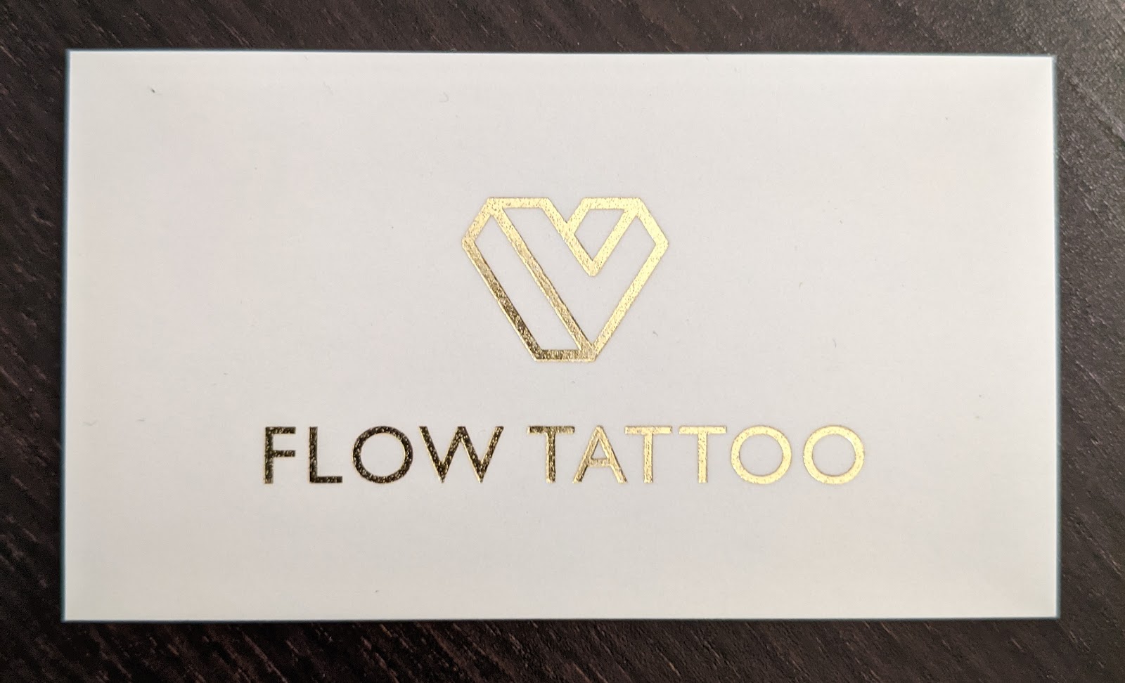 White business card with a gold foil heart logo on a dark wood table