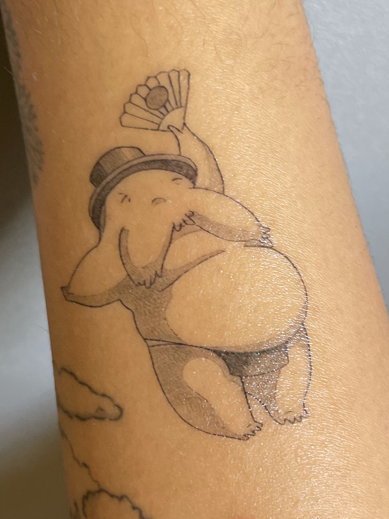 Fine line blackwork tattoo of a round character with a top hat and a fan, on a forearm