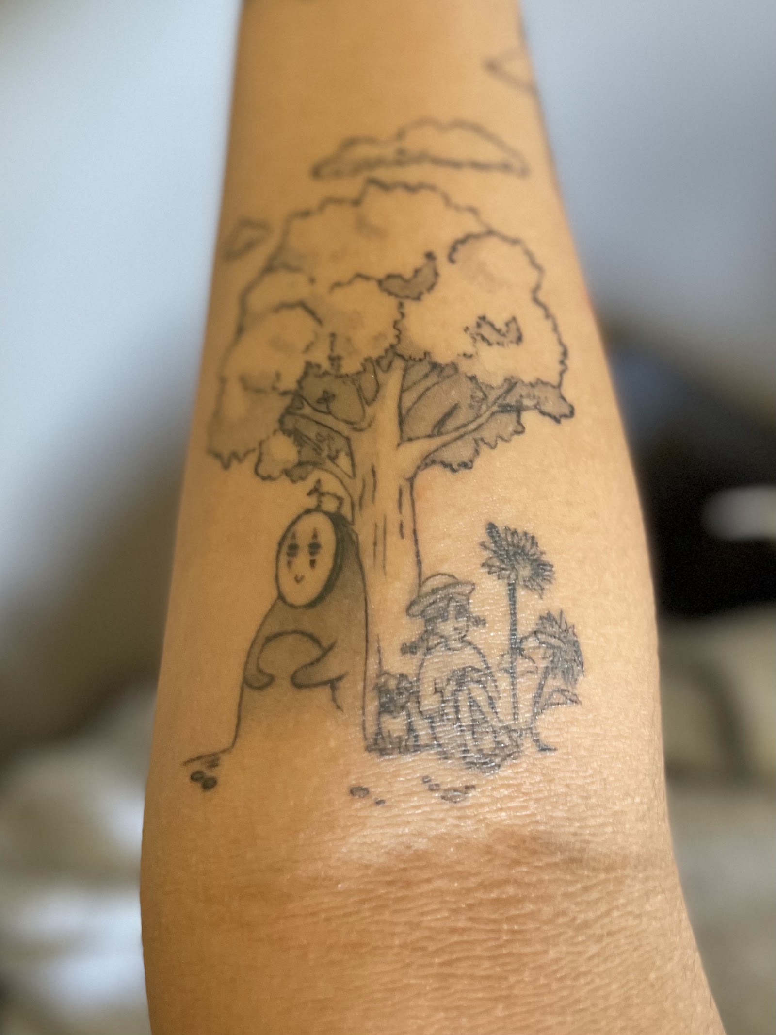 Blackwork forearm tattoo of a tree with a masked spirit and a girl among flowers
